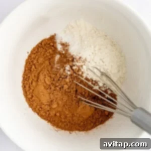 Banana Bread Brownie Mashup 7 A white bowl with cocoa powder, flour, and baking soda being mixed with a metal whisk.