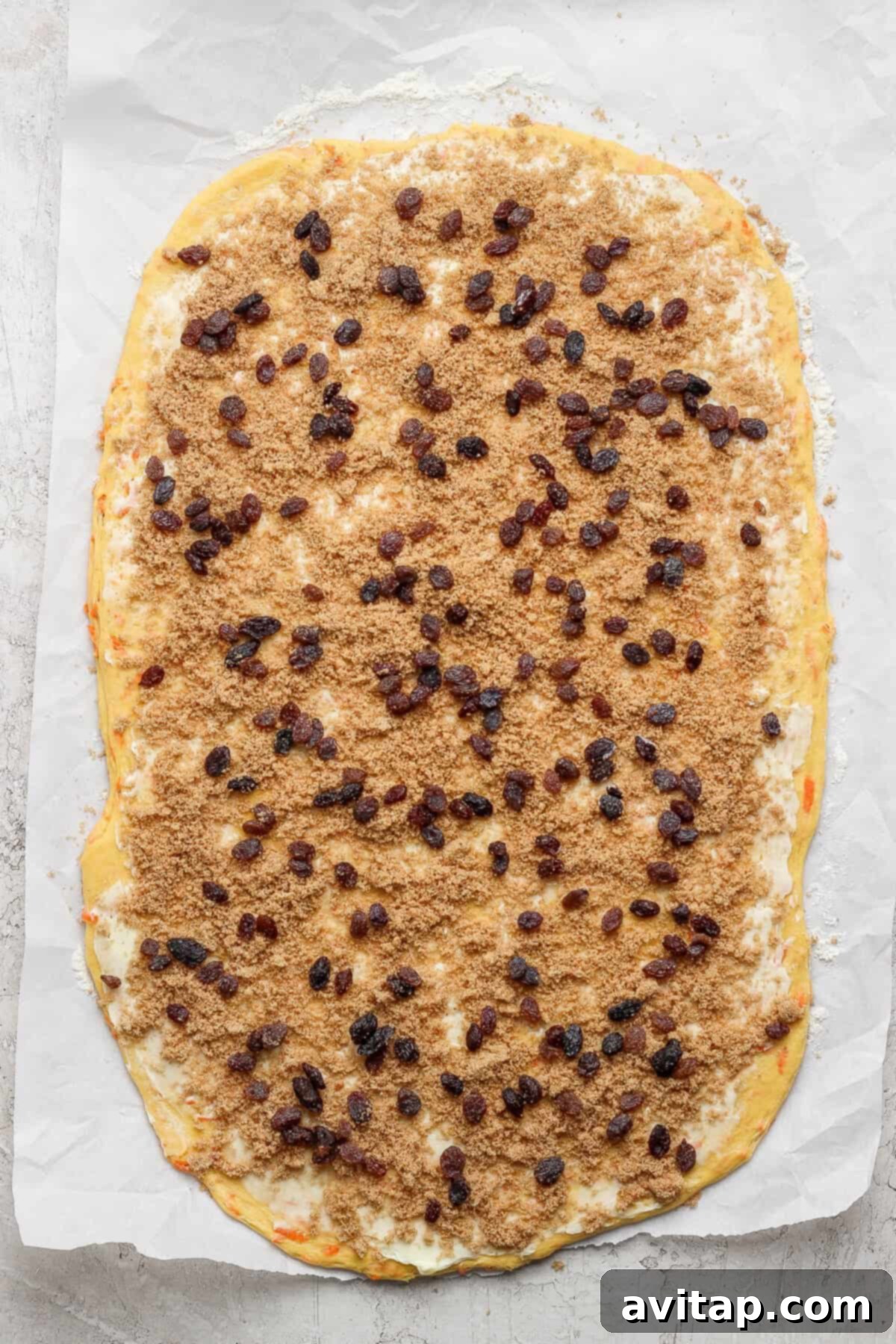 Carrot Cake Cinnamon Swirls 3 The rectangular dough on parchment paper, kissed with brown sugar and raisins, stands ready to be rolled into delightful carrot cake cinnamon rolls, showcasing the filling before rolling.