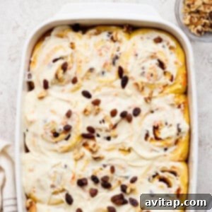 Carrot Cake Cinnamon Swirls 7 A baking dish filled with frosted carrot cake cinnamon rolls, topped with raisins and walnuts. A small bowl of walnuts is nearby, completing the delicious picture.