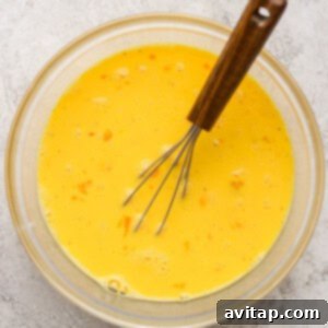 A whisk blending eggs, cottage cheese, and half and half in a glass bowl, creating the custard base for the casserole.