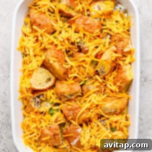 A white baking dish filled with the casserole, now topped with shredded cheddar cheese, ready for the final baking stage.