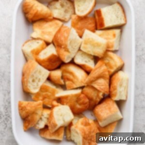 A white baking dish filled with bite-sized croissant pieces on a textured surface.