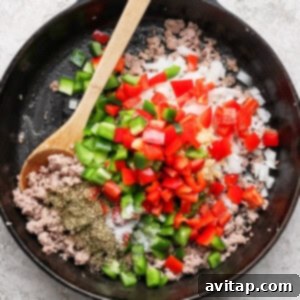 A cast iron skillet filled with browned ground sausage, chopped red and green bell peppers, diced onions, and garlic, seasoned with herbs.