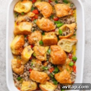 A baking dish containing a mixture of browned croissant pieces, ground sausage, and brightly colored diced bell peppers, ready for the egg mixture.
