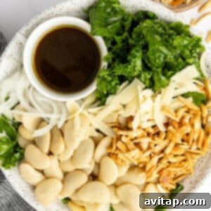 A salad bowl containing chopped kale, sliced white onions, butter beans, shredded cheese, toasted slivered almonds, and a small dish of dark dressing.