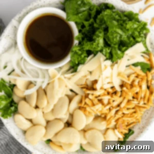 A plate with butter beans, sliced onions, kale, shredded cheese, toasted slivered almonds, and a small cup of dark dressing.