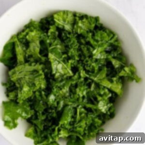 A white bowl filled with fresh, chopped kale leaves on a light marble surface.