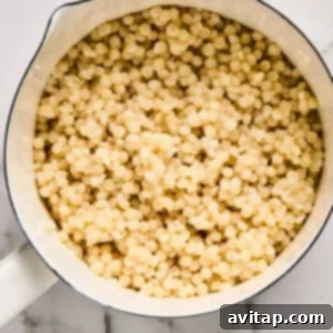 A pot filled with perfectly cooked pearl couscous, glistening and ready for further preparation, resting on a pristine marble surface.