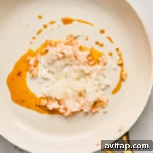 Minced white onions sizzling gently in sun-dried tomato oil within a white frying pan, placed on a elegant marble countertop, beginning to soften.