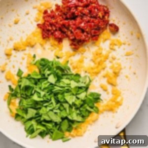 Vibrant chopped spinach and sun-dried tomatoes being tossed with sautéed onions in a frying pan on a smooth marble surface, as the spinach wilts.