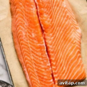 A raw salmon fillet laid on parchment paper, expertly prepped with a central cut for stuffing, a sharp knife resting beside it on a marble surface.