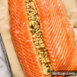 A raw salmon fillet on parchment paper, beautifully split open and generously filled with a flavorful mixture of couscous, herbs, and spices, ready for baking.