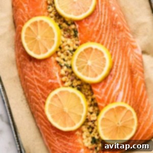 A raw salmon fillet, perfectly stuffed with seasoned breadcrumbs and elegantly topped with fresh lemon slices, rests on parchment paper, ready for the oven.