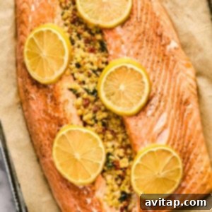 A golden-brown baked salmon fillet, generously stuffed with a flavorful couscous mixture and adorned with bright lemon slices, rests on a parchment-lined baking sheet, fresh from the oven.