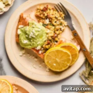A beautifully plated baked salmon, richly topped with a vibrant green sauce, elegantly served alongside fluffy couscous, crumbled feta cheese, and bright lemon slices. A fork rests on the plate, ready to enjoy.