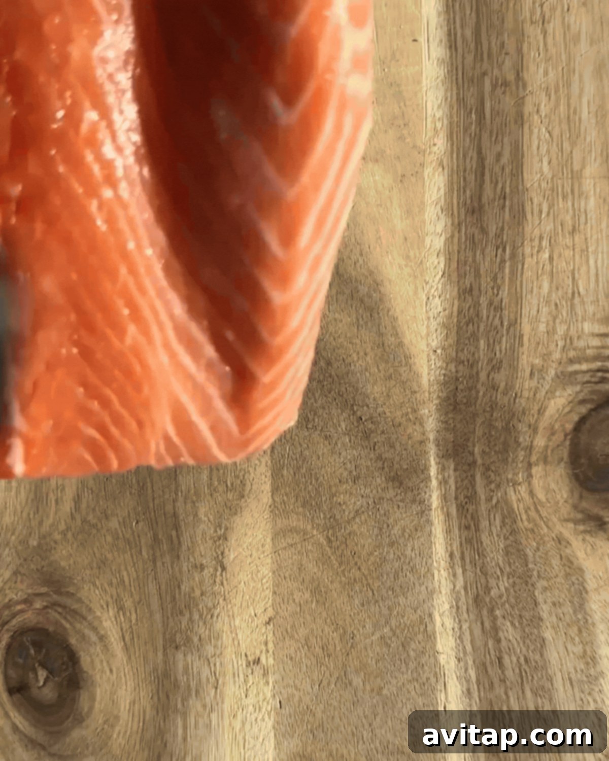 Chef's hands carefully slicing a large, raw salmon fillet lengthwise to create a pocket for stuffing, demonstrating the precise technique.