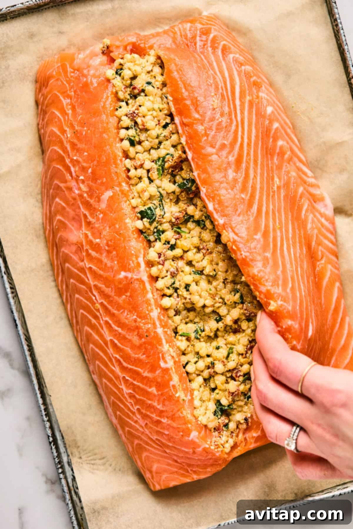 Raw salmon fillet, expertly slit open to reveal a deep pocket, ready to be filled with a flavorful mixture of herbs and grains, resting on parchment paper on a baking tray.