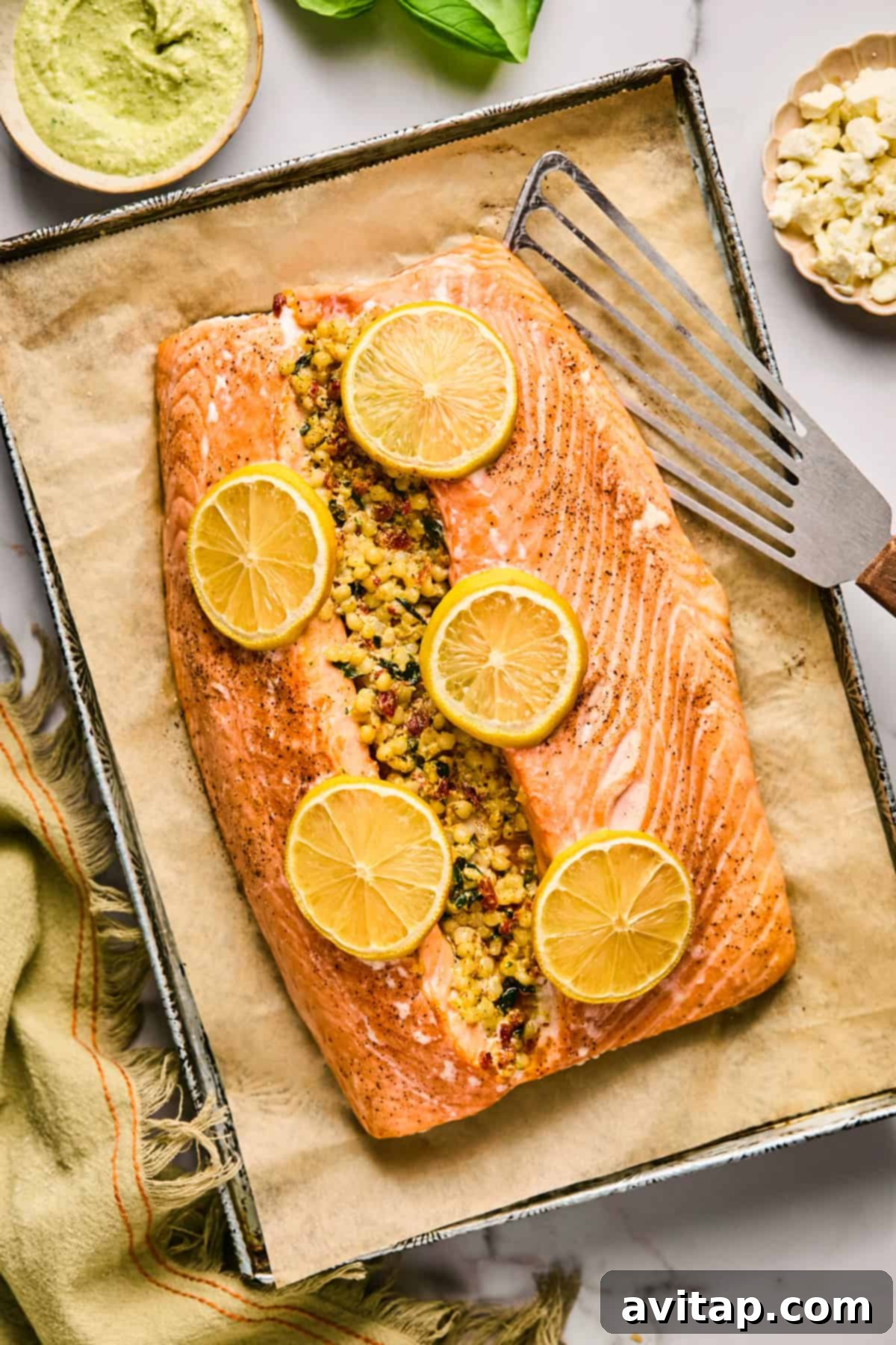 A perfectly baked salmon fillet, generously stuffed with a flavorful couscous mixture and garnished with vibrant lemon slices, presented on a parchment-lined baking tray with a serving spatula beside it.