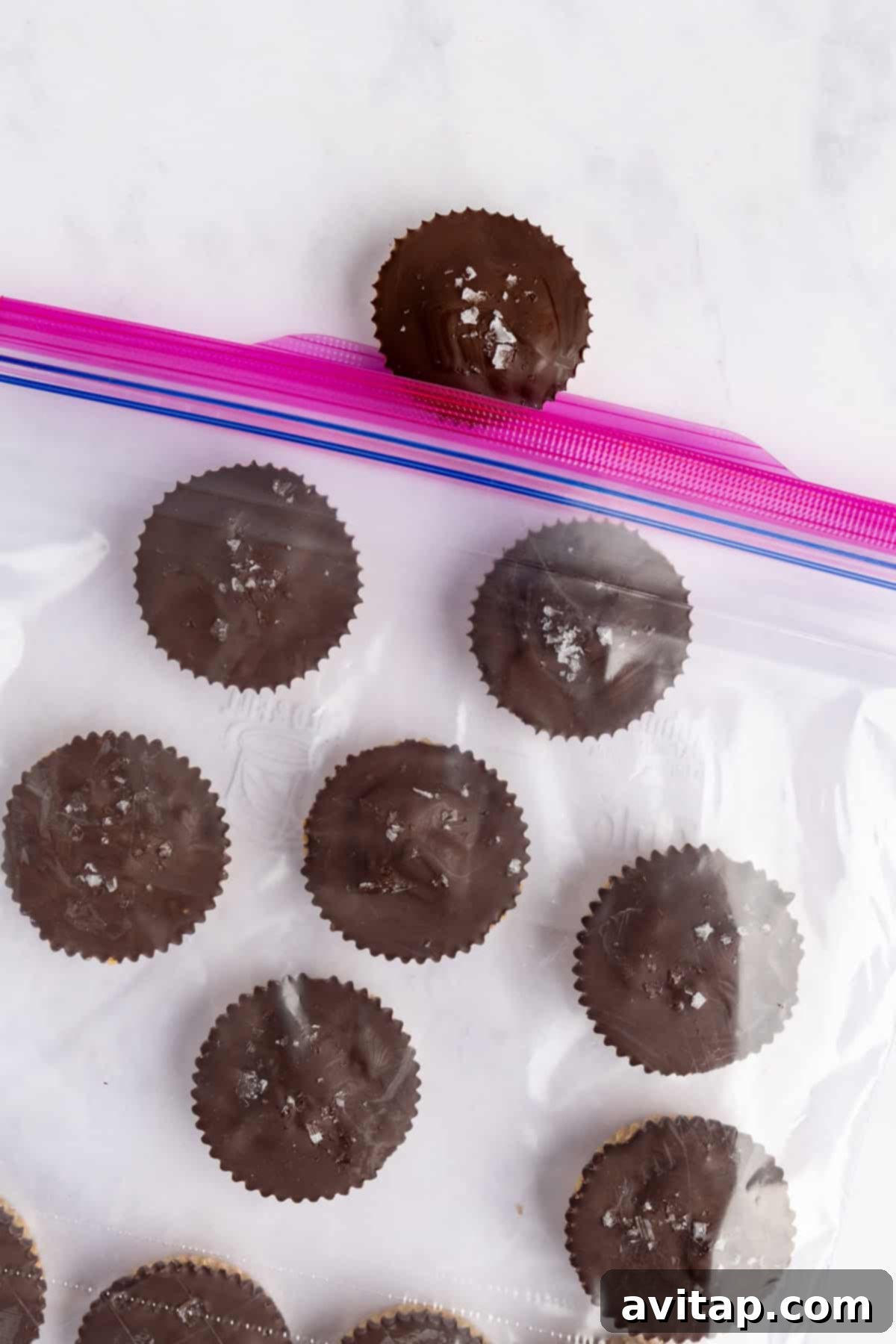 Chocolate-covered peanut butter cups, some sprinkled with sea salt, neatly arranged inside a transparent resealable freezer bag, with one cup placed artfully outside the bag.