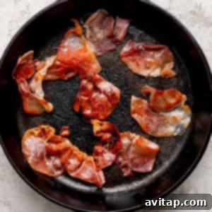 Several slices of perfectly cooked prosciutto, golden brown and crispy, resting in a black cast iron skillet on a light textured countertop surface.