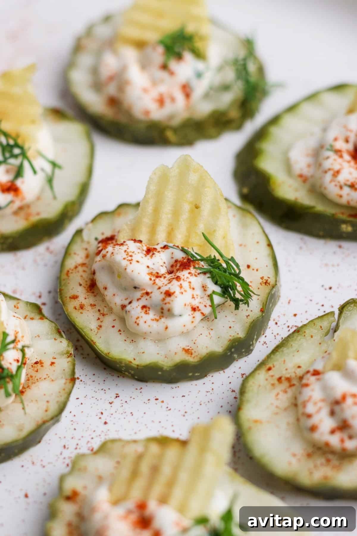Cucumber slices topped with creamy dip, a potato chip, dill, and sprinkled with paprika.
