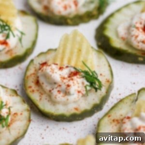 Cucumber slices topped with sour cream, a potato chip, dill, and paprika on a white surface.