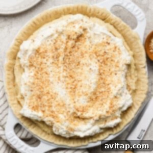 A freshly prepared pie, elegantly topped with creamy whipped cream and sprinkled with golden toasted coconut flakes, rests on a light-colored surface alongside a serving knife and a neatly folded striped cloth.