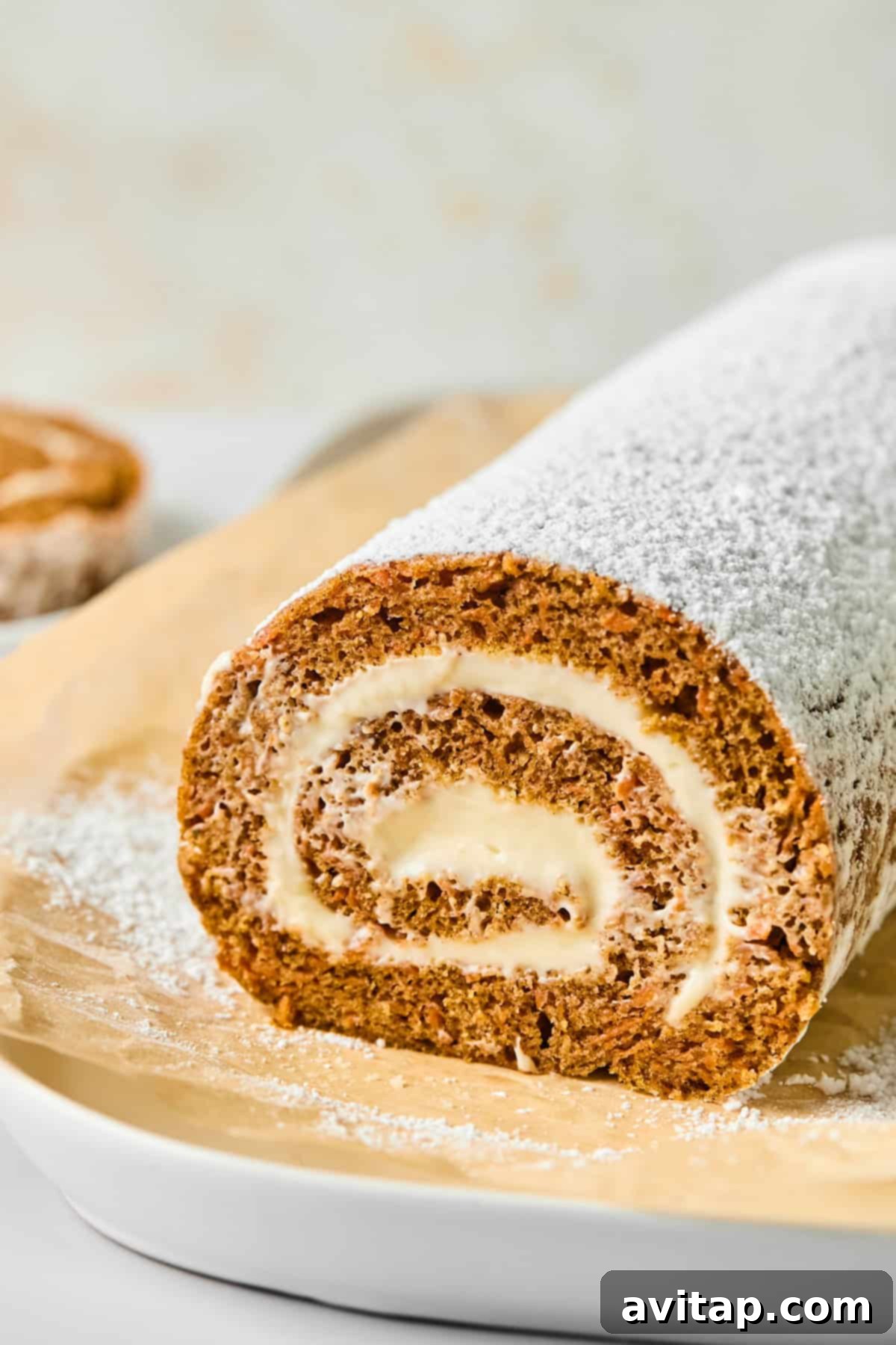 A beautifully rolled carrot cake dusted with powdered sugar, showcasing a perfect spiral of creamy filling on parchment paper.