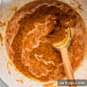 A white bowl filled with a frothy, orange mixture, and a wooden spoon partially immersed in the liquid, resting against the side.