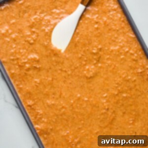 Baking tray filled with raw carrot cake batter and a spatula resting on top.