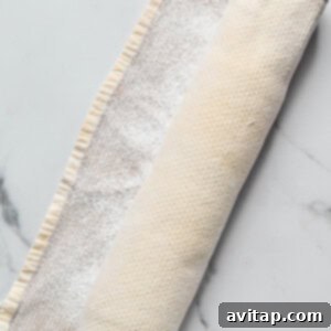 Rolled-up dough wrapped in a floured kitchen towel on a marble surface.
