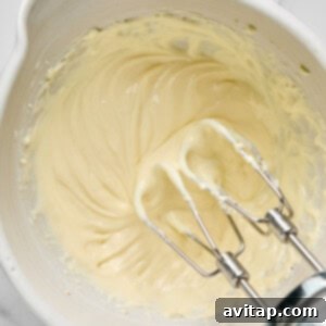Electric mixer beaters in a bowl with creamy batter on a marble countertop.
