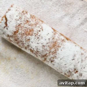 A rolled cake dusted with powdered sugar rests on a textured cloth.