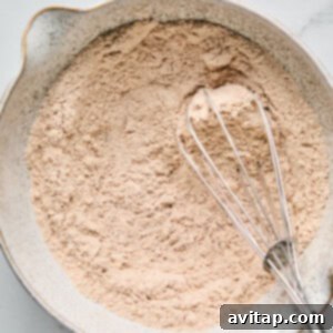 A bowl of dry ingredients is mixed with a metal whisk on a marble surface.