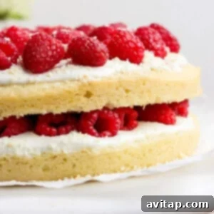 Layered cake with white frosting and fresh raspberries on a cake stand.