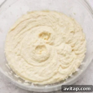 A glass bowl filled with creamy, light yellow cake batter on a textured white surface.