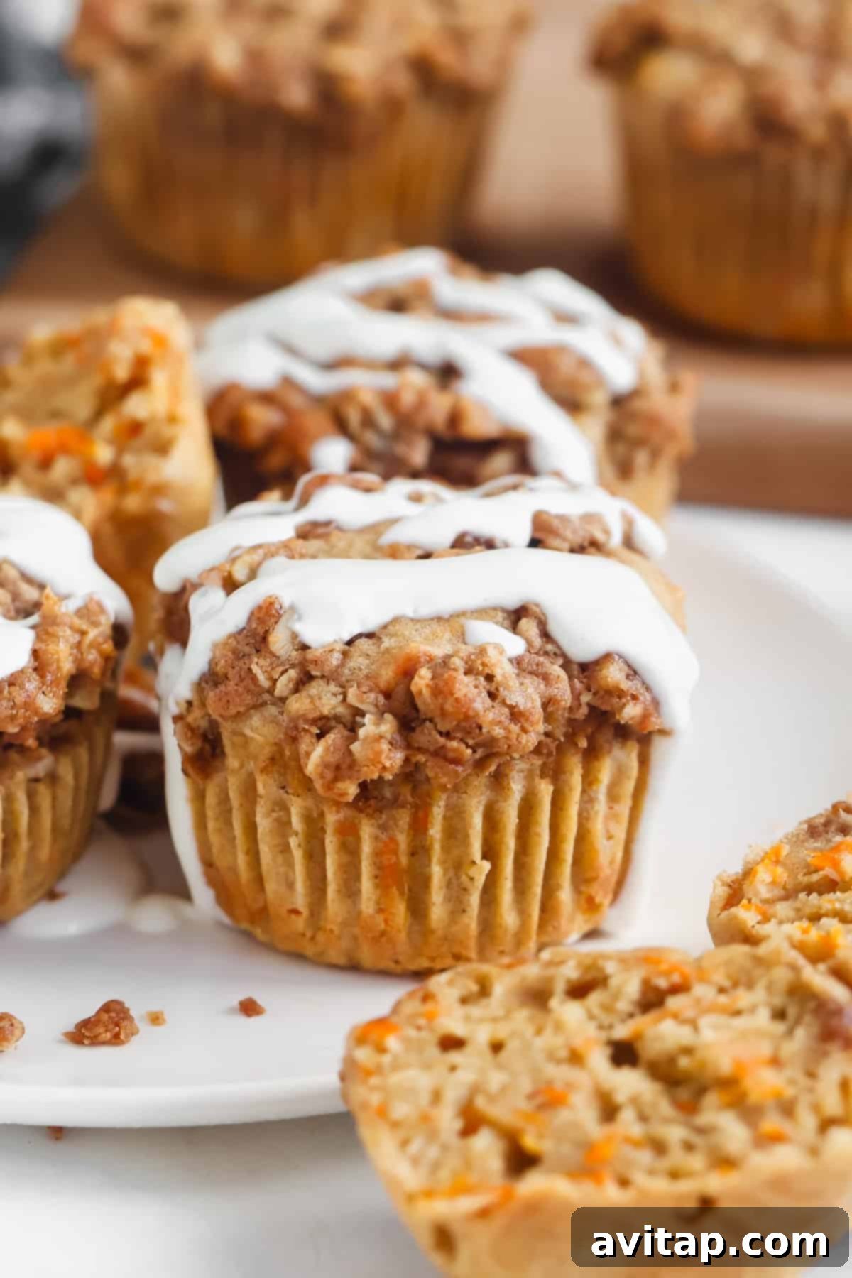 Delicious Cottage Cheese Carrot Cake Muffins with a crumbly streusel topping and creamy white icing, arranged invitingly on a plate. One muffin is cut in half, revealing its moist, carroty interior.