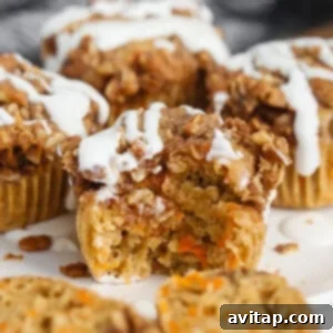 Close-up of a perfectly baked carrot muffin with a golden crumbly topping and a delicate white icing drizzle, with a bite taken out.