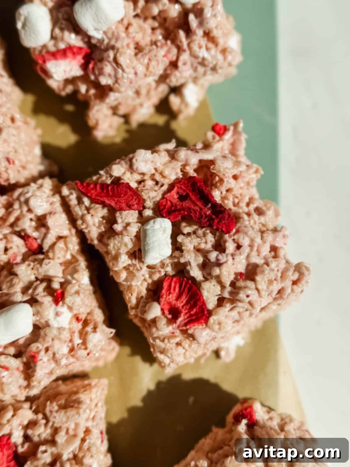 Close-up of cereal treats with red dried fruit pieces and small marshmallows on a light surface.