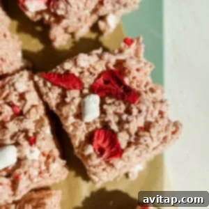 Rice crispy treat square with red dried strawberries and small marshmallows on a green and beige surface.