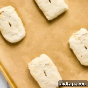 Four unbaked biscuit dough pieces, reminiscent of bubbling pizza crusts, rest on a parchment-lined baking sheet.