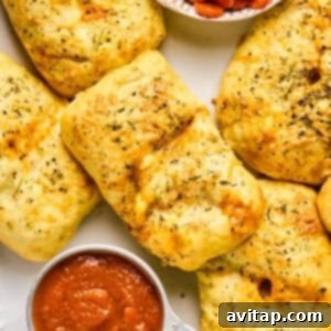 Golden, herb-seasoned bread parcels resembling mini pizza hot pockets sit beside a small dish of sliced pepperoni and a cup of marinara sauce.