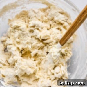 A glass bowl containing partially mixed dough with a wooden spoon sits ready to become delicious homemade pizza or hot pockets.