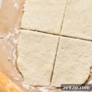 Rolled-out dough on parchment paper, cut into four sections like the perfect start for homemade pizza pockets, with a wooden rolling pin nearby.
