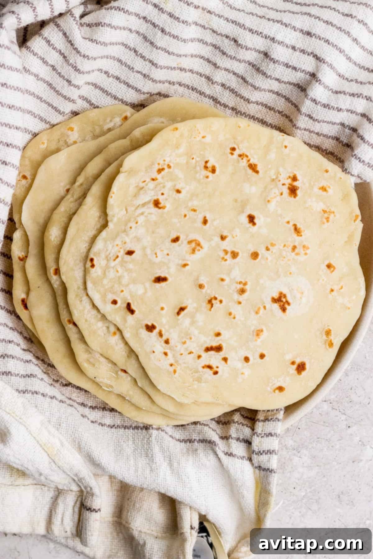 A stack of golden-brown homemade protein tortillas resting on a rustic striped kitchen towel, warm and ready to be enjoyed.