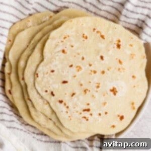 A stack of homemade flour tortillas rests on a striped kitchen towel.