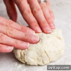 Hands expertly kneading a soft ball of dough on a lightly floured countertop, preparing it for rolling.