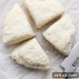 Four small, uniform balls of dough, along with a knife, resting on white parchment paper, ready to be rolled into tortillas.