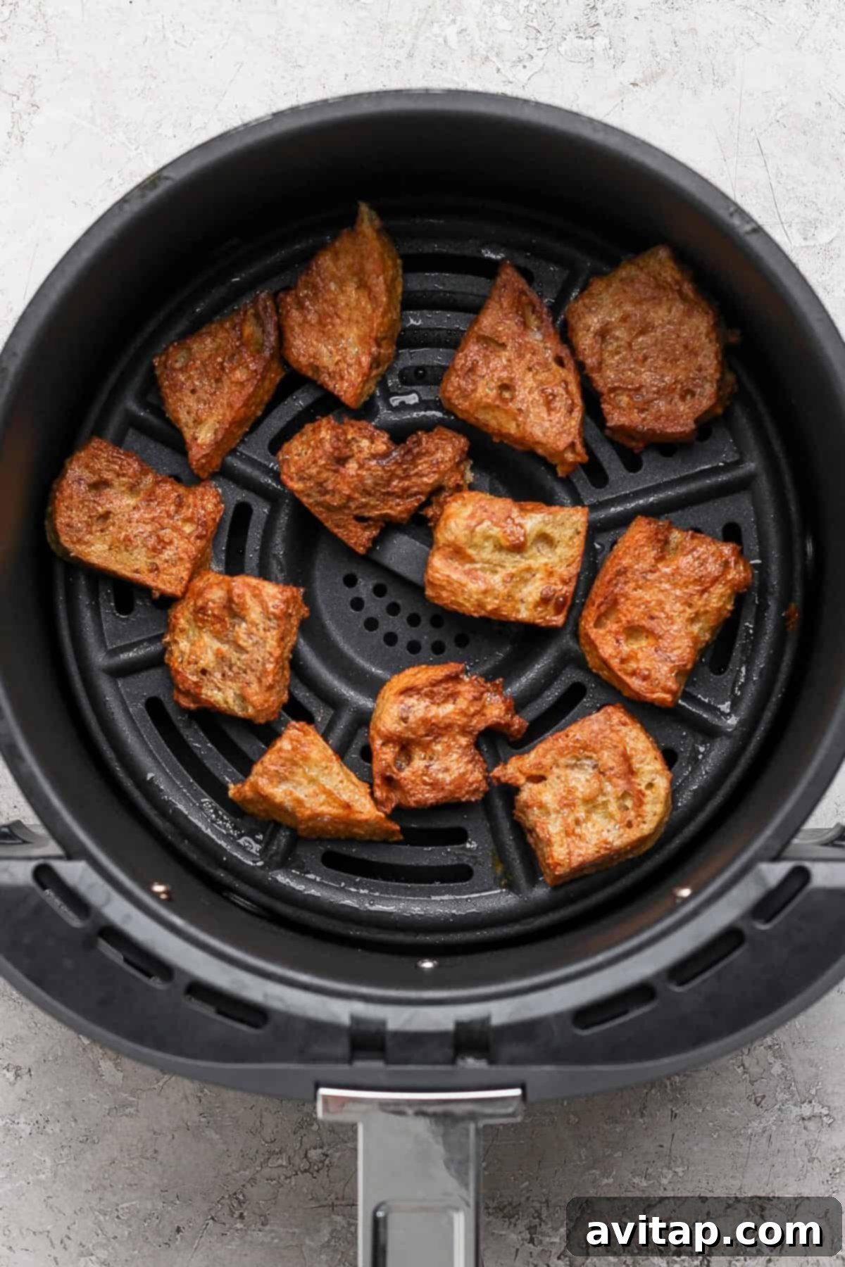 Crispy, golden-brown French toast bites resting in an air fryer basket after cooking, showcasing their perfect texture.