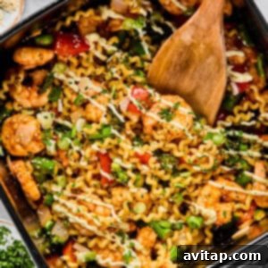 Crispy Air Fryer Shrimp & Veggies 4 A pan filled with cooked pasta, shrimp, vegetables, and herbs being stirred with a wooden spatula, showcasing the saucy and vibrant dish.